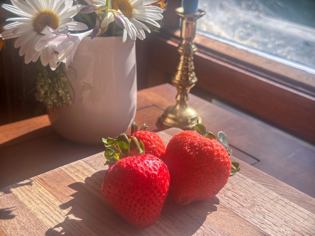 three big red strawberries on a wood cutting board
