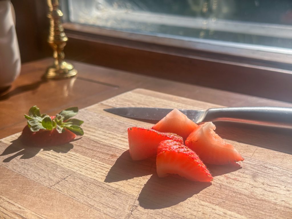 cut up strawberry on cutting board with knife 